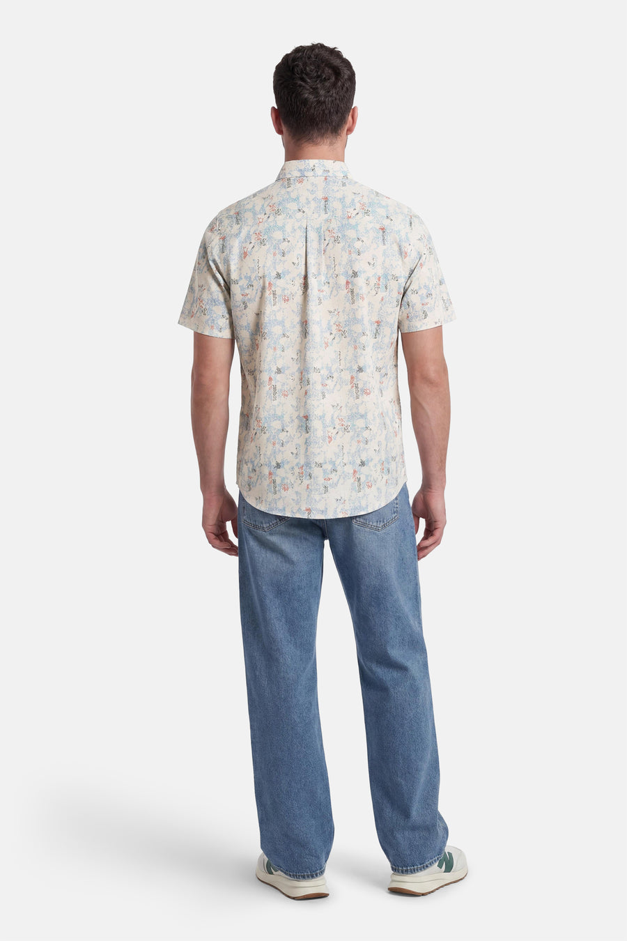Chemise multicolore à manches courtes de TOM TAILOR, portée dans le dos, avec motif abstrait bleu et orange, associée à un jean bleu ample et des baskets blanches.