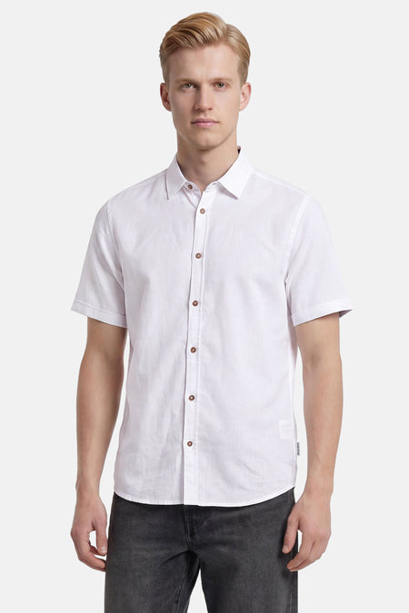 Chemise blanche à manches courtes de TOM TAILOR, avec des boutons marron, portée par un homme avec un jean gris.