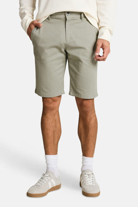 Shorts verts TOM TAILOR en tissu uni, avec une poche passepoilée et des passants de ceinture, vus de dos sur un homme portant une chemise gaufrée de couleur crème et des baskets blanches.