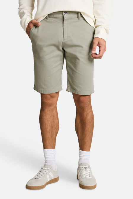 Shorts verts TOM TAILOR en tissu uni, avec une poche passepoilée et des passants de ceinture, vus de dos sur un homme portant une chemise gaufrée de couleur crème et des baskets blanches.