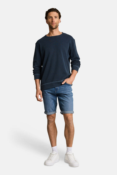 Jeansshort van denim in middenblauw, van TOM TAILOR, gecombineerd met een donkerblauw shirt, witte sokken en witte sneakers.
