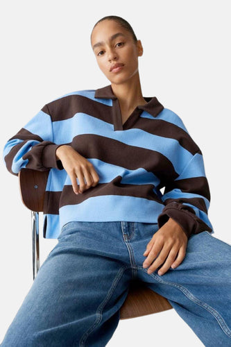 Vrouw in blauw en bruin gestreepte trui en jeans.
