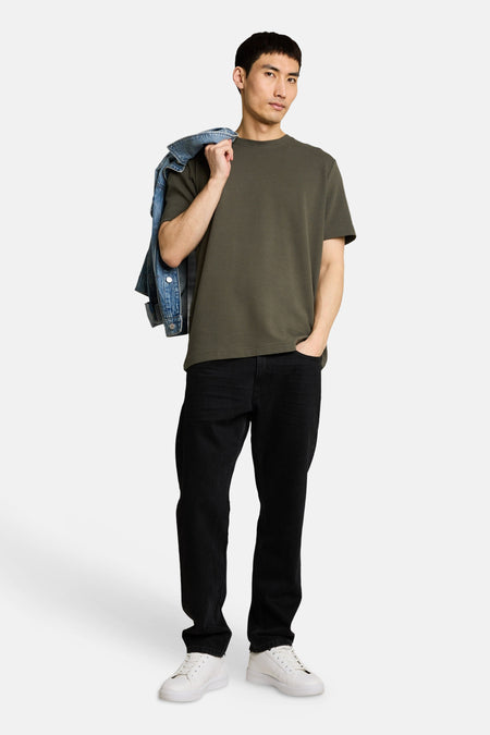 Kaki T-shirt met korte mouwen van TOM TAILOR, met subtiele ribstructuur, gedragen door een man met zwarte jeans en witte sneakers.