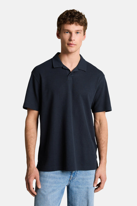 Polo bleue de TOM TAILOR, portée sur un t-shirt blanc à manches longues et un bermuda en jean clair.