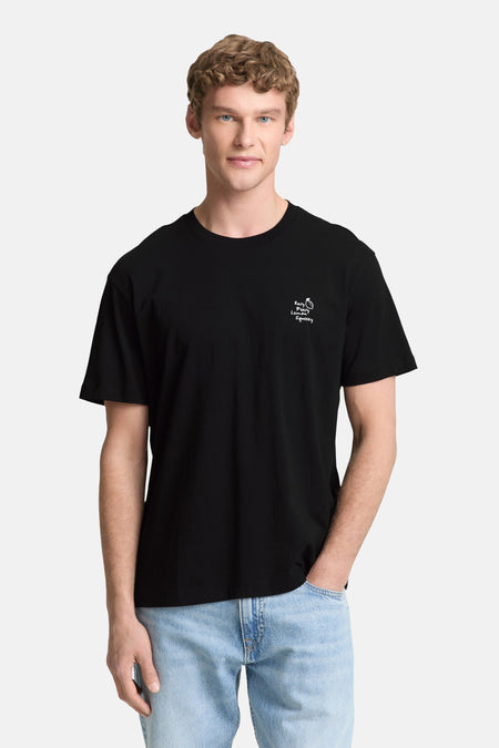 T-shirt noir à manches courtes de TOM TAILOR, avec une veste en jean sur l'épaule, combiné avec un jean bleu clair et des baskets blanches.