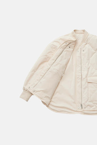 Manteau court beige d'OPUS, avec motif losange et fermeture éclair argentée, ouvert sur fond blanc.