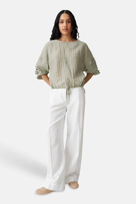 Groene blouse met lange mouwen van OPUS, met een aansnoerkoord en gedragen met een witte pantalon.
