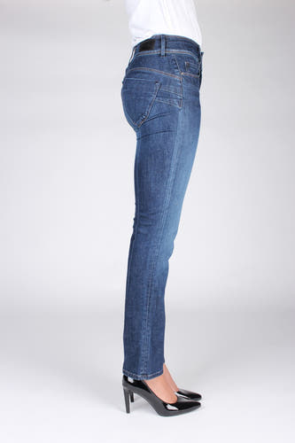 Femme debout, jeans bleus, chaussures noires, chemise blanche.