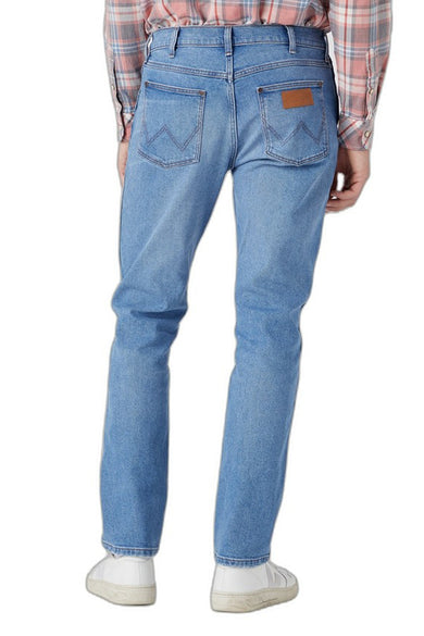 Blauwe tapered jeans van Wrangler, met bruin leren label op de achterzak en gedragen met een geruit overhemd.