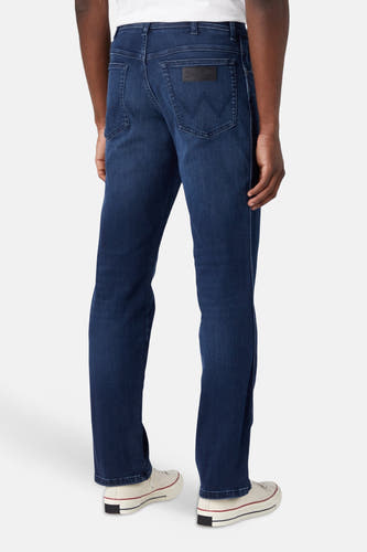 Achteraanzicht van donkerblauwe straight jeans van Wrangler® met zwarte patch en 'W'-stiksels op de achterzakken, gedragen met witte sneakers.