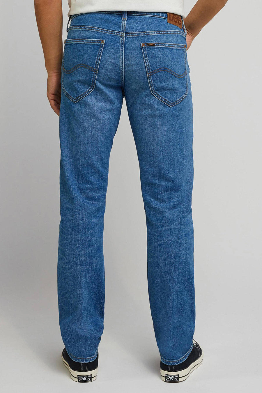 Rechte jeans van blauw denim van Lee®, gezien vanaf de achterkant, met donkere sneakers.
