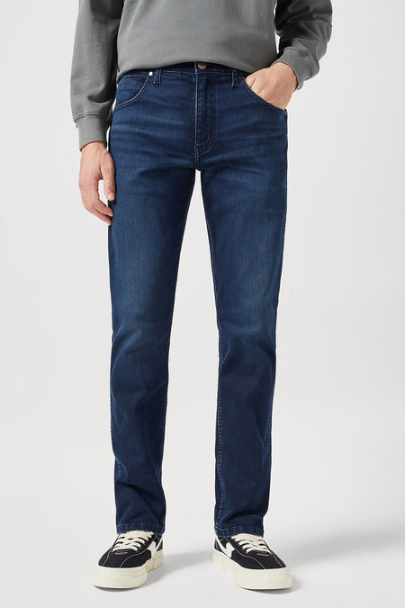 Jean droit bleu foncé Wrangler, dos, avec étiquette de marque en cuir et combiné avec un pull gris et des baskets blanches.