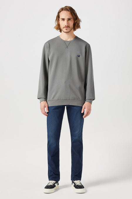 Donkerblauwe rechte jeans van Wrangler, gecombineerd met een grijze sweater en zwarte lage sneakers.
