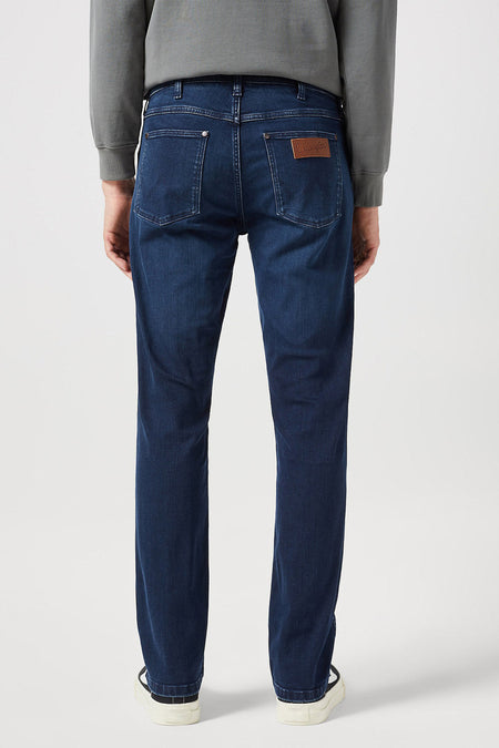 Donkerblauwe rechte jeans van Wrangler, achterkant, met leren merklabel en gecombineerd met grijze sweater en witte sneakers.