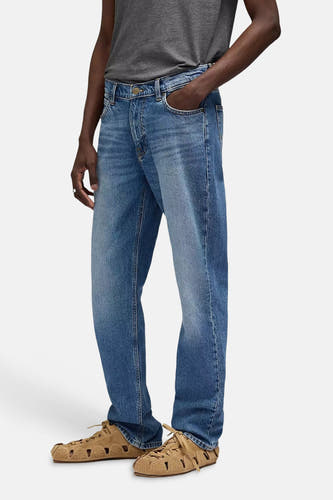 Jean droit en denim bleu de Lee®, stylé avec un t-shirt gris et des sandales marron.