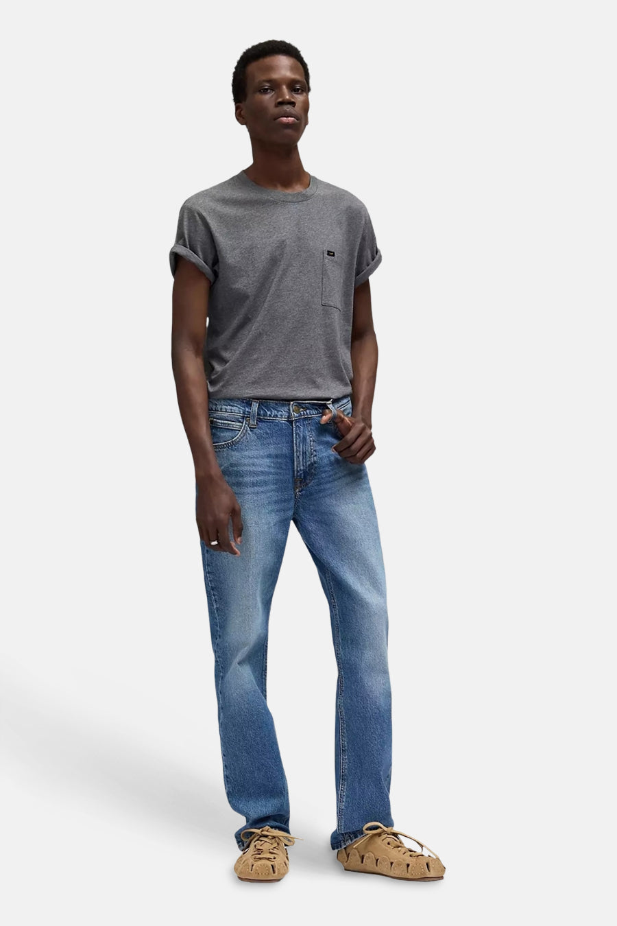 Jean droit en denim bleu de Lee®, associé à un t-shirt gris et des chaussures en daim.