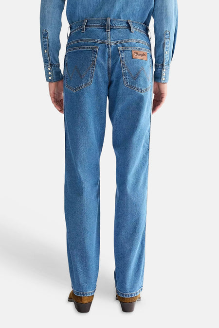 Rechte spijkerbroek van mid-blauw denim van Wrangler, met W-stiksels op de achterzakken en leren patch, van achteren gezien.