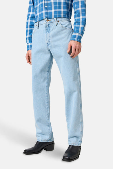 Jean droit en denim bleu clair de Wrangler, avec des poches cousues et une chemise à carreaux colorée.