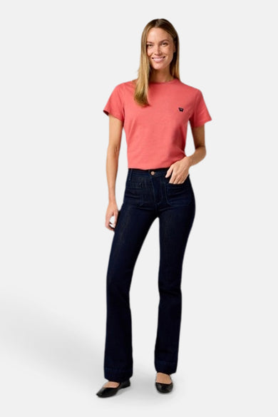 Jean flare bleu marine denim de Wrangler®, associé à un T-shirt corail et des baskets noires.
