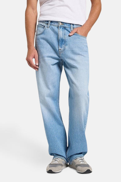 Jean décontracté de denim bleu clair de Lee, avec une coupe ample et des baskets grises.