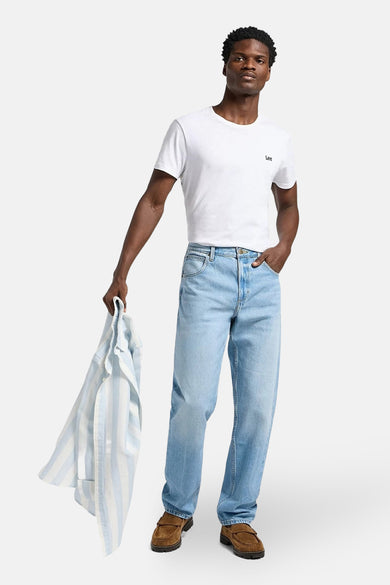 Boutons de jeans en denim bleu clair de Lee, avec un T-shirt blanc et des chaussures en cuir marron.