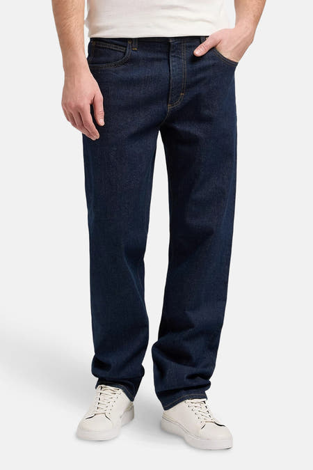 Jean tapered bleu marine de Lee, avec surpiqûres dorées et baskets blanches.