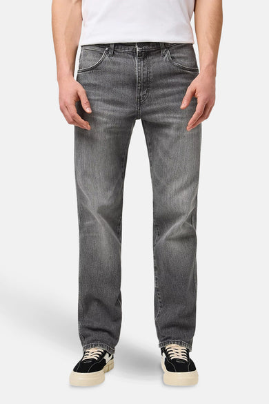 Jean Wrangler large large couleur gris foncé, avec poche et main visible.