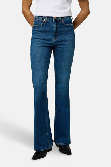 Jeanon denim bleu délavé évasés de Wrangler®, avec une taille haute et des chaussures noires.