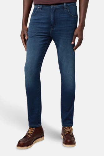 Jean en denim bleu marine tapered de Wrangler, porté avec des bottes en cuir marron à boucles.