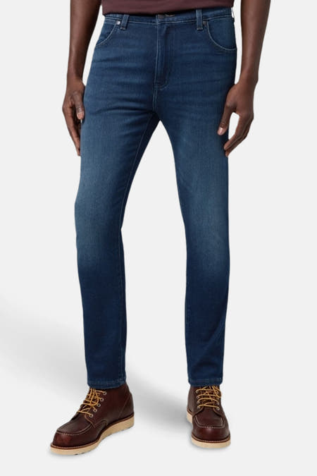 Jean en denim bleu marine tapered de Wrangler, porté avec des bottes en cuir marron à boucles.