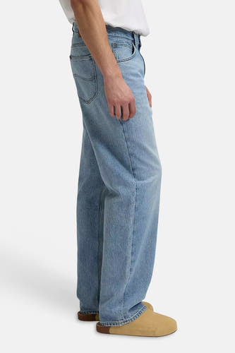 Jean large bleu clair de Lee®, porté avec un t-shirt blanc et des sabots beiges, vue de côté.