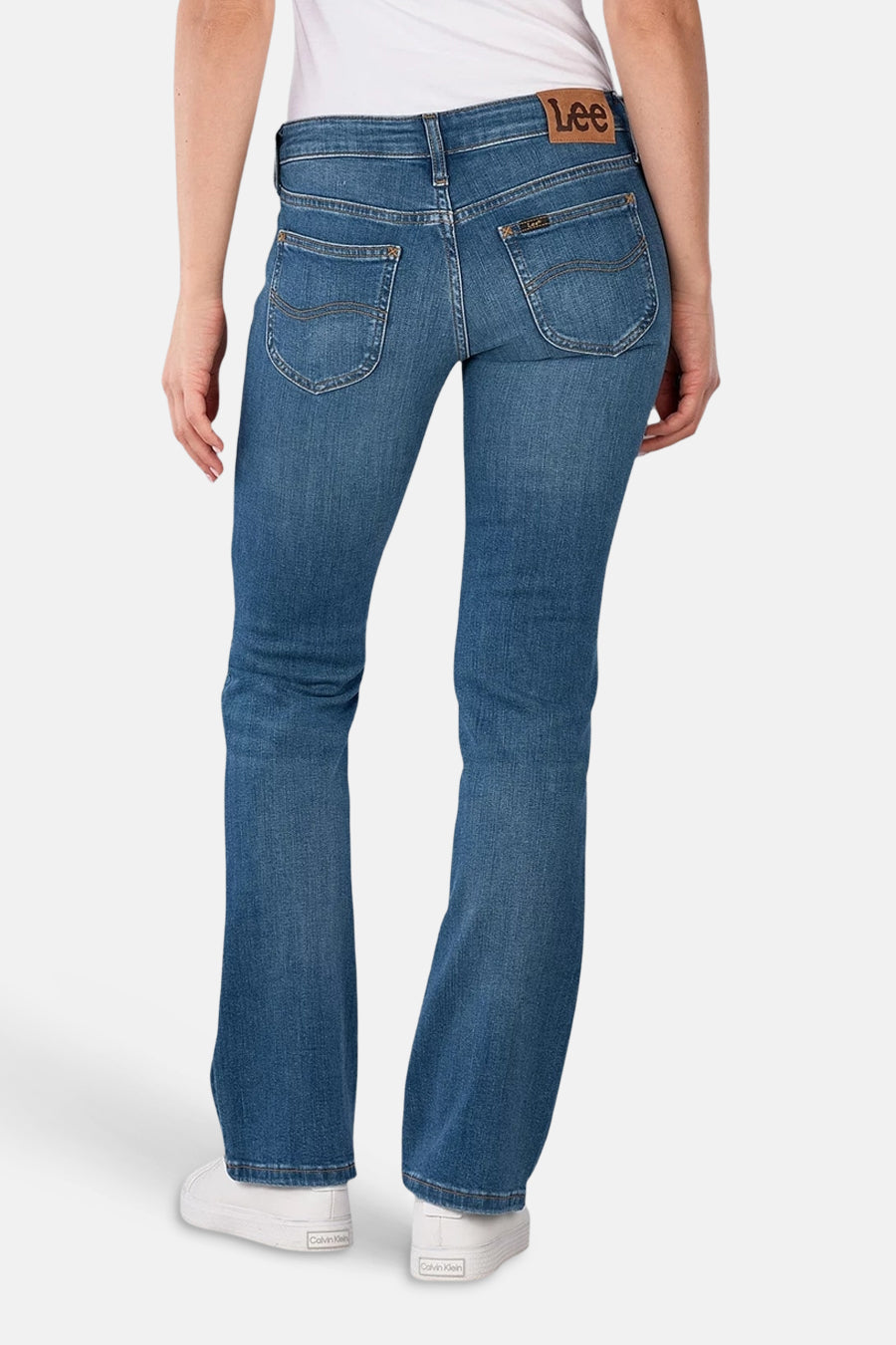 Middenblauwe bootcut jeans van Lee, met sierlijke achterzakken en witte schoenen.
