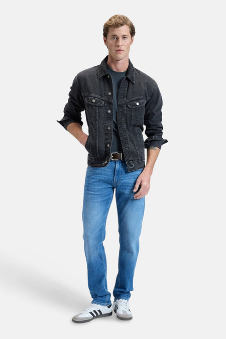 Jean droit bleu DAREN de Lee, avec une ceinture marron et des baskets blanches.