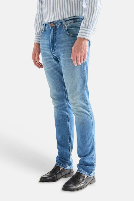 Jean droit en denim bleu clair de Wrangler avec surpiqûres en « W » sur la poche arrière et étiquette en cuir, porté avec une chemise rayée et des mocassins.