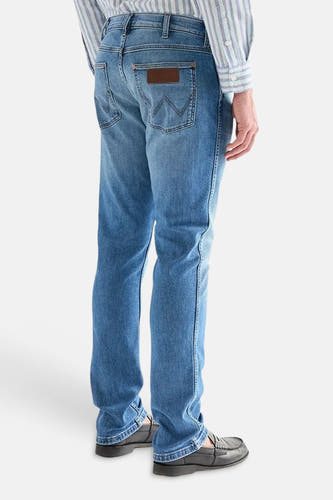 Lichtblauwe denim straight jeans van Wrangler met 'W'-stiksels op de achterzak en leren label, gedragen met een gestreept overhemd en loafers.