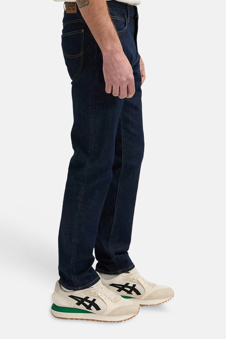 Donkerblauwe tapered jeans van Lee®, zijprofiel, met contrasterende naden en beige sneakers met groene zool.