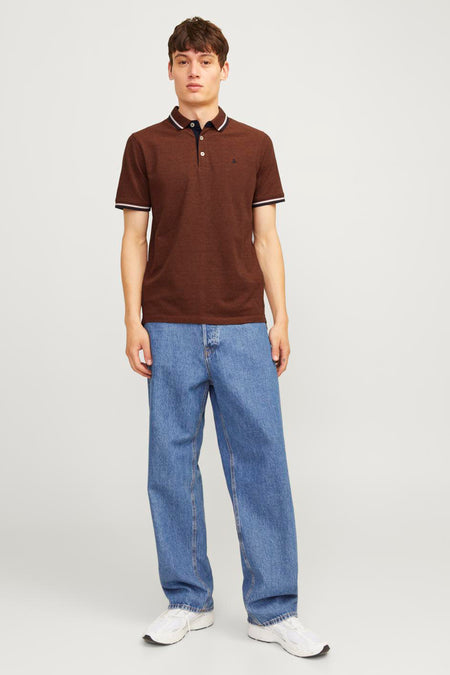 Man met bruine polo, wijde jeans en witte sneakers.