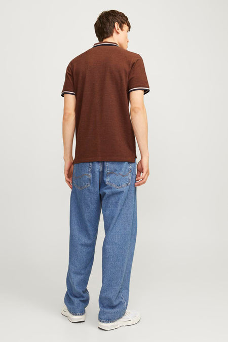 Achterkant van een man in een bruin poloshirt, wijde blauwe jeans en witte sneakers.