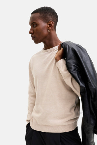 Man met beige trui en zwarte leren jas over de schouder.