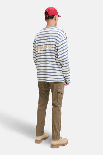 Pantalon de travail brun de JACK & JONES JEANS INTELLIGENCE, avec des poches et porté avec un t-shirt rayé et une casquette rouge.