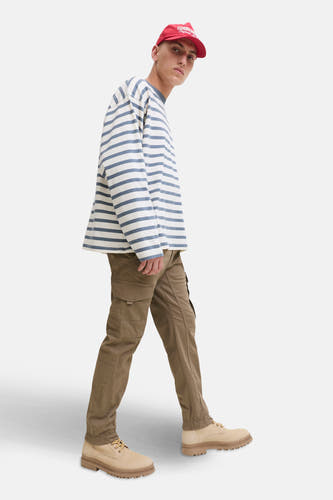 Pantalon cargo brun de JACK & JONES JEANS INTELLIGENCE, associé à un pull rayé, une casquette rouge et des baskets beige.