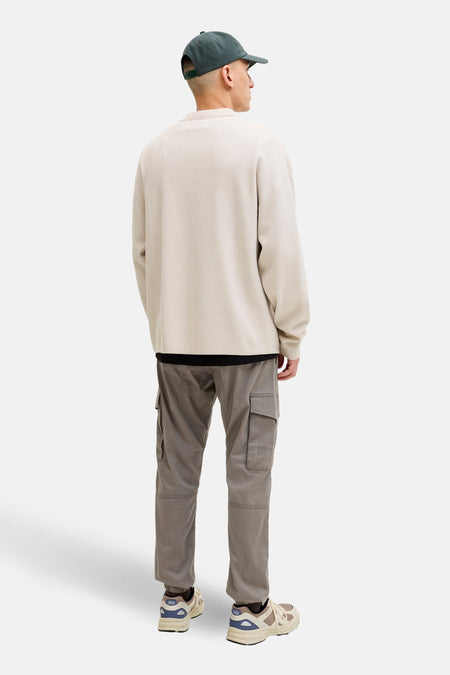 Man van achteren, beige sweater, grijze cargobroek, groene pet, crèmekleurige sneakers.
