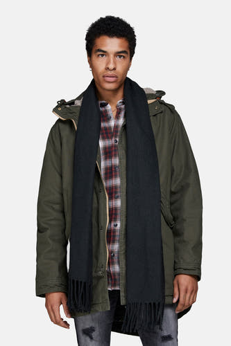 Chapeau d'hiver noir d'ACCESSORIES BY JACK & JONES, avec franges, porté avec un chemisier à carreaux et une parka.