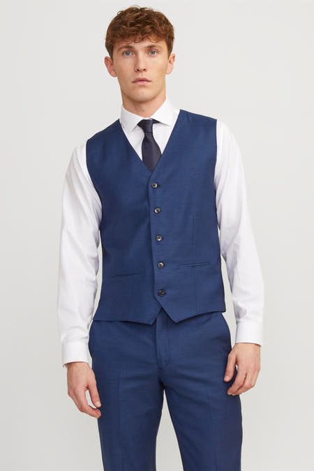 Gilet bleu de PREMIUM par JACK & JONES, avec une ceinture ajustable sur le dos, associé à un chemisier blanc et un pantalon bleu.
