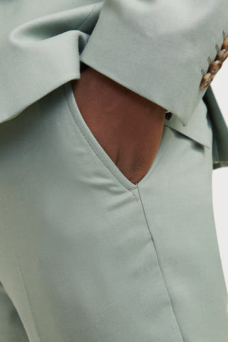Pantalon de costume vert de PREMI by by JACK & & J, avec une main dans la poche et des boutons sur les manches.