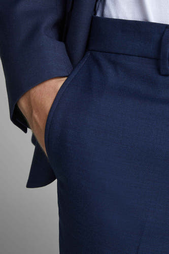 Pantalon de costume bleu PREMIUM by JACK & JONES, avec une main dans la poche et une subtile texture.