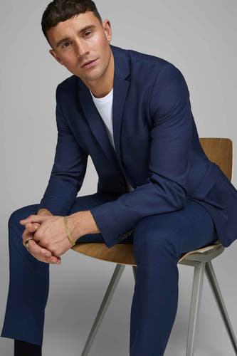 Pantalon de costume bleu PREMIUM by JACK & JONES, porté avec un T-shirt blanc et une bague en or, assis sur une chaise en bois.