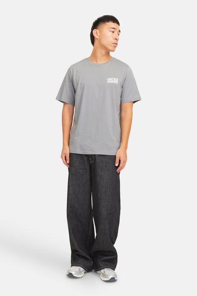 T-shirt gris à manches courtes de CORE par JACK & JONES, avec petit logo sur la poitrine, associé à des jeans larges et des baskets.