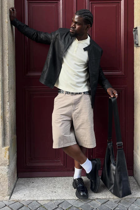 Veste de motard noire en cuir avec détails zippés, de CORE BY JACK & JONES, portée en pose lifestyle devant une porte rouge