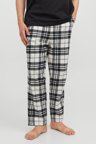 Pantalon de pyjama noir et blanc d'ACCESSORIES BY JACK & JONES, à motif à carreaux, porté avec un t-shirt noir et pieds nus.